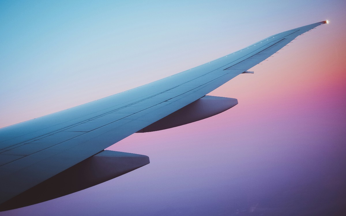 Airplane wing seen from the window against a pastel sunset sky.