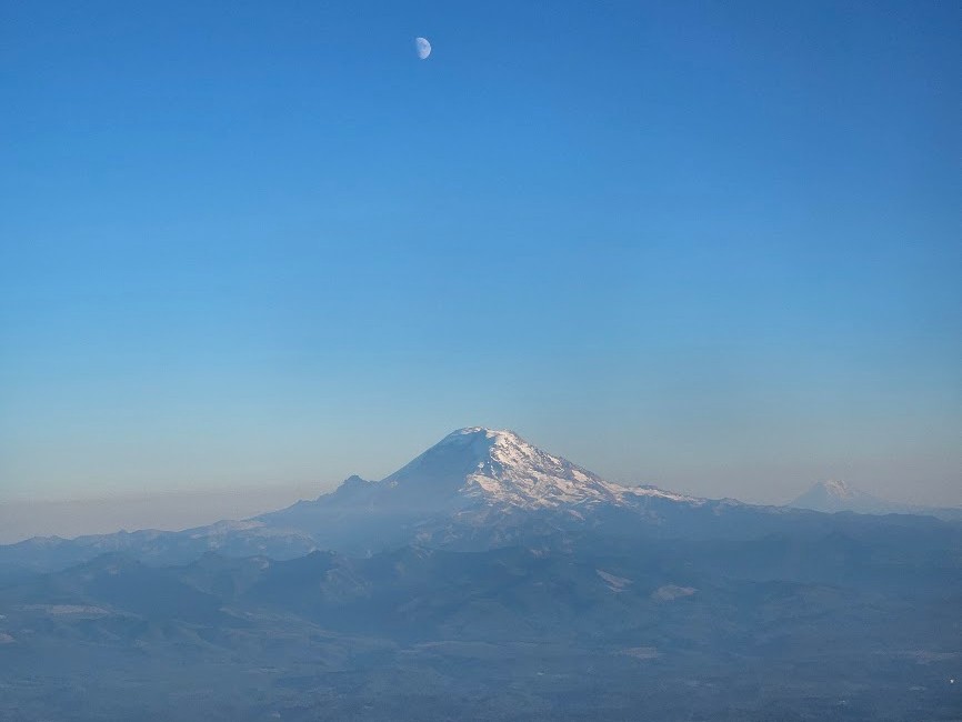 Snow-covered mountain peak under a clear blue sky with a crescent moon above the summit.