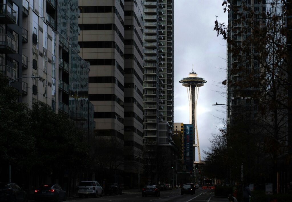 Seattle Space Needle rising between tall city buildings along a street.