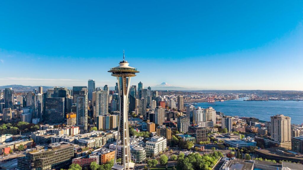 Aerial view of downtown Seattle with the Space Needle, high-rise buildings, and Puget Sound under a clear blue sky.