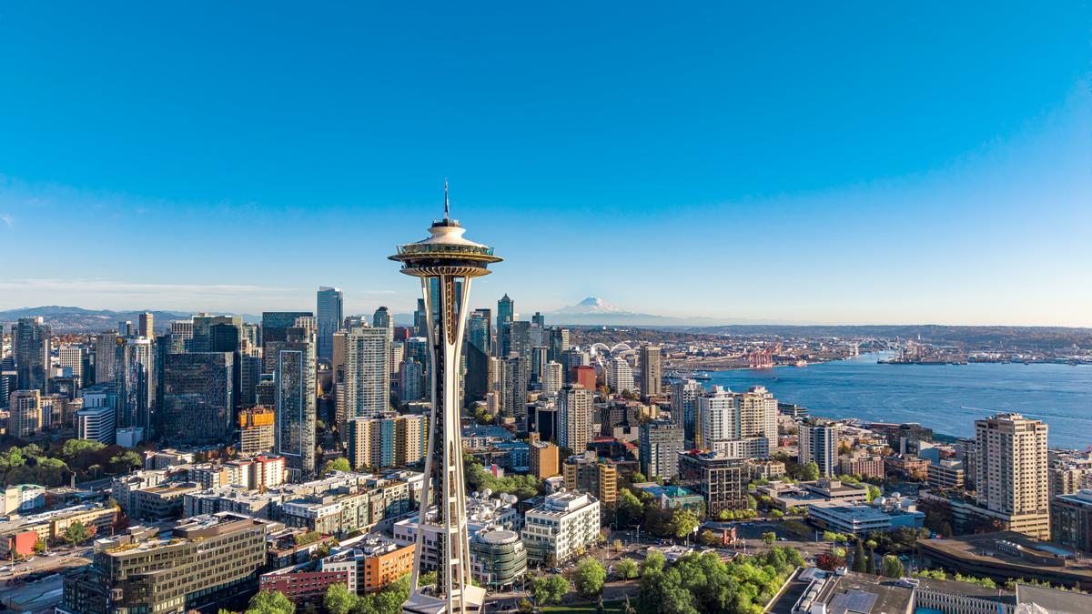 Aerial view of downtown Seattle with the Space Needle, high-rise buildings, and Puget Sound under a clear blue sky.