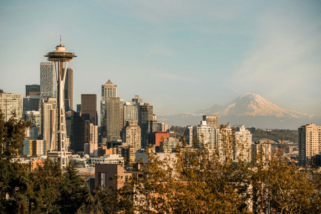 Seattle skyline with the Space Needle in the foreground, downtown skyscrapers nearby, and Mount Rainier on the distant horizon under a clear sky.