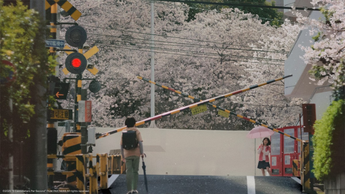 Railway crossing on a street with striped barriers and a red light; a person walks away with a backpack, cherry blossoms in bloom, a girl with a pink umbrella nearby.