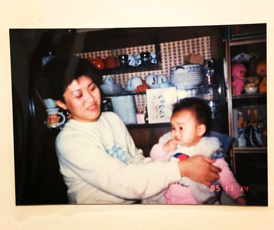 Woman in a light sweater holding a baby among shelves of ceramic dishes and pottery in a shop/kitchen setting.