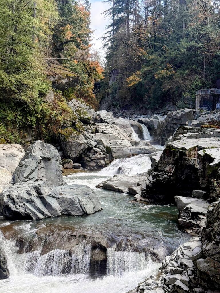 granite-falls-fish-ladder-1 - junglecity.com Rugged river gorge with cascading waterfalls over layered gray rocks and autumn foliage above the water.
