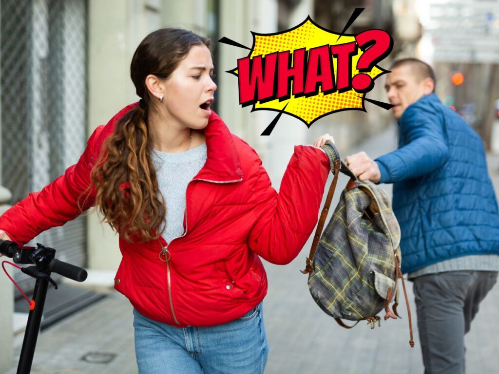 Woman in a red jacket pulls away a plaid backpack on a city sidewalk as a man in a blue jacket approaches; a bright 'WHAT?' comic graphic overlays the scene.